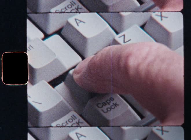 Super 8mm closeup of the finger of an unrecognisable man or person pressing the shift key on the gray keyboard of an old vintage computer with retro design in order to start a program or process of the operating system or OS