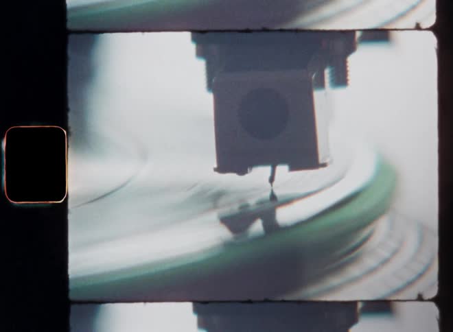 Dynamic film footage closeup of the spinning or turning edge of a Technics SL-1210 turntable as the needle touches down on the reflecting surface of the vinyl record and slides into place so that the music is played on Super-8