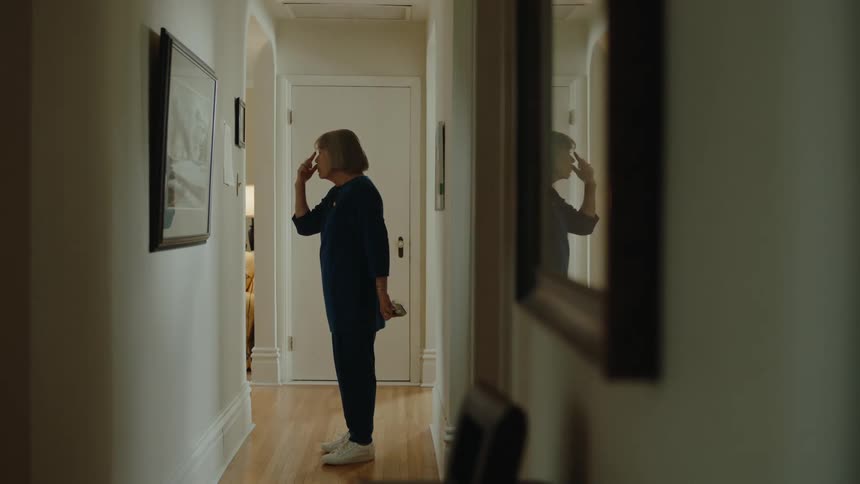 Older woman attaches paper to the hallway wall and focuses on it