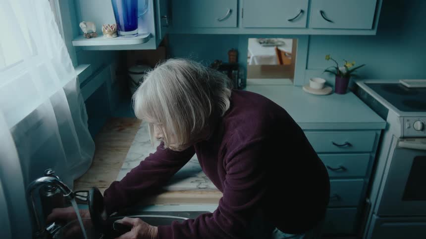 Elderly lady in the kitchen picking up a coffee kettle and pouring water