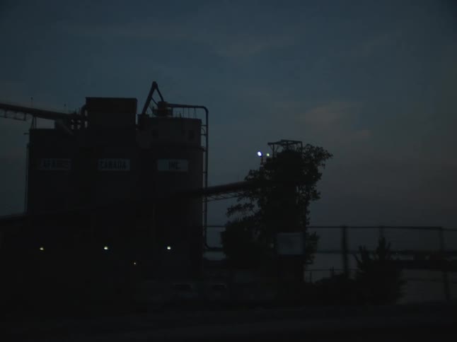 A car drives by a grain storage facility by a river