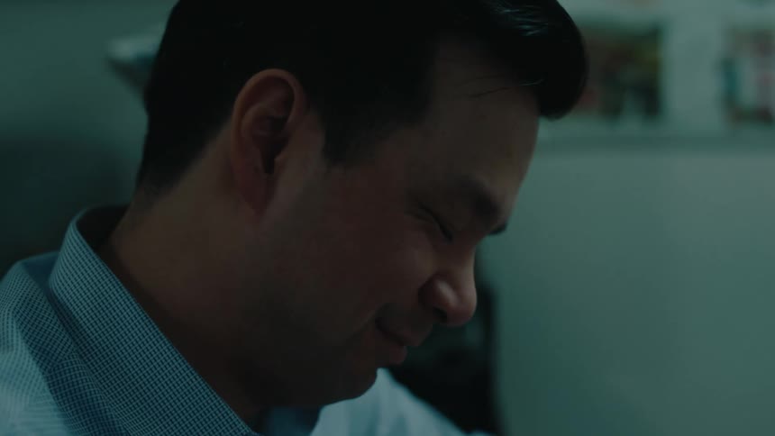 A doctor sits in his office smiling and listening