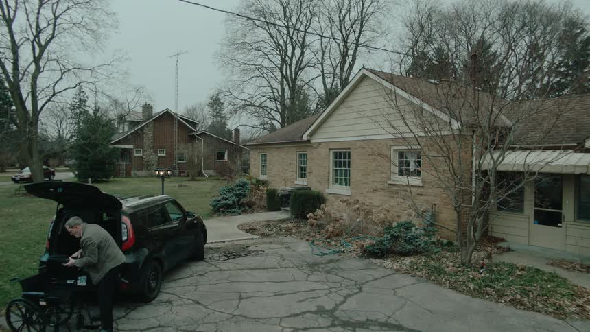 Man takes a wheelchair out of the trunk of a car parked in the driveway