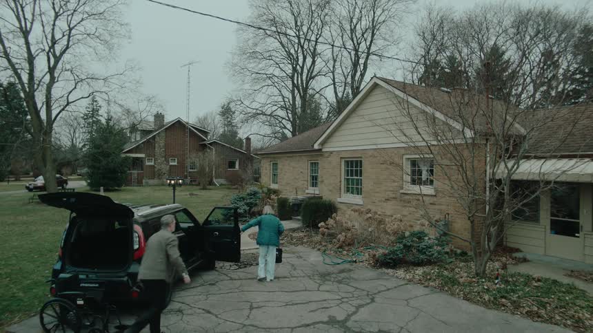 A man helps his ill mother walk into her house on a winter day