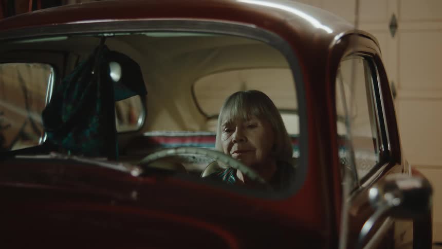 An elderly female sitting at the wheel of a car in a garage