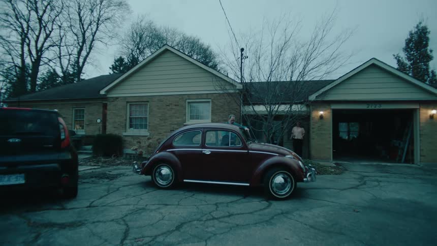 Man running out of the garage towards a beetle and helping a lady out of the car