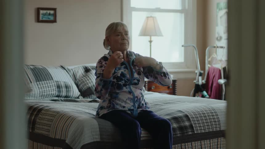 An elderly woman is sitting on a bed and stretching her arms