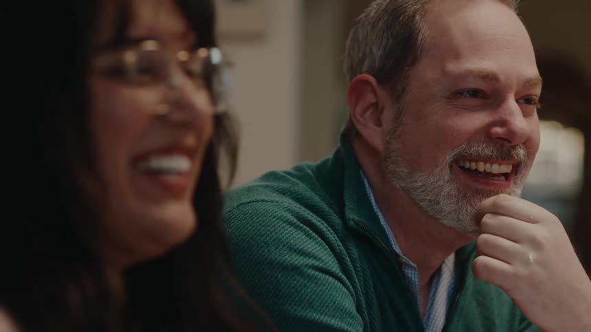 Man and woman sitting at table smile while talking with friends