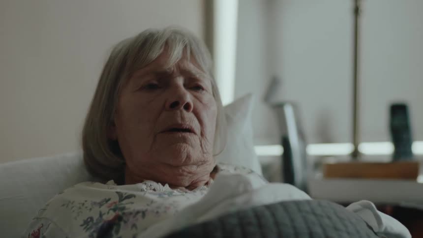 An elderly woman looks sad as she collapses into her bed