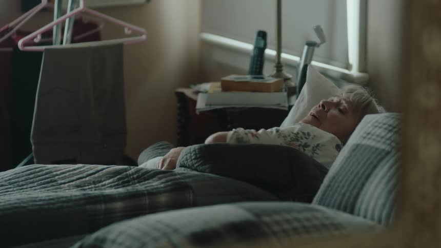 An elderly woman is lying on a bed using a blanket and then getting up