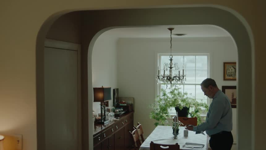 A man standing at the dining room table opening his mail after work