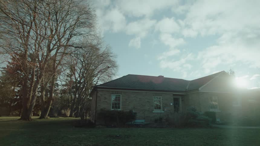 A brick house sits near bare trees as the sun shines over the roof