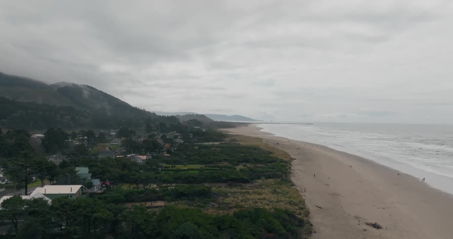 The cloudy sky casts a shadow over a long beach with calm waves