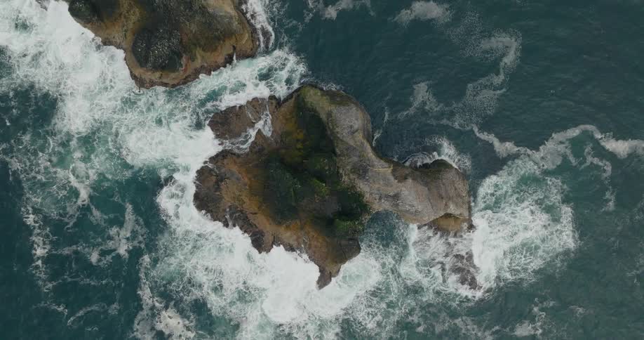 View from above of eroded rocks in the middle of the blue sea with strong waves