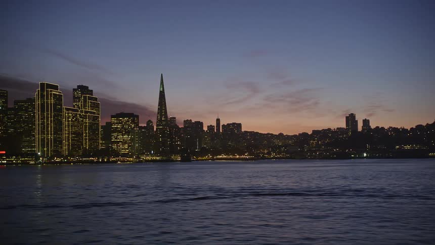 A view of a city skyline at night with the empire state building prominently lit in the center
