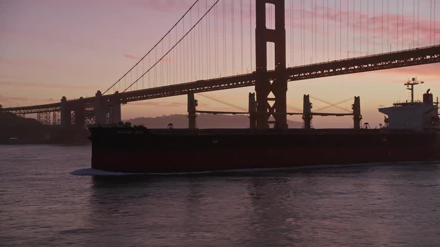 Cargo ship passing below the golden gate bridge in a reddish sky