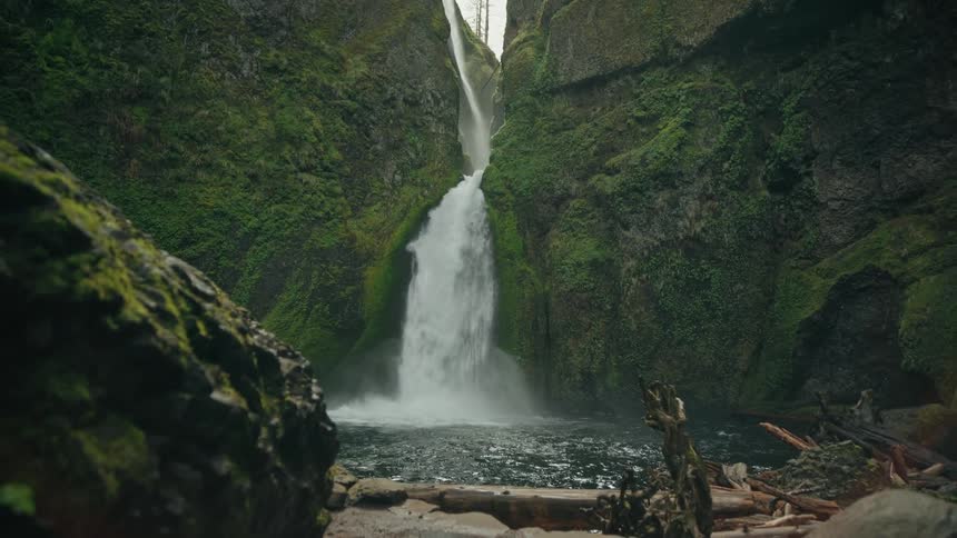 Waterfalls flow over a moss covered cliff into the stream below