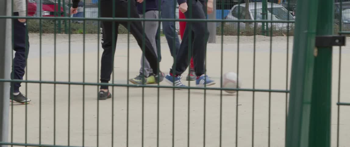 A group of people behind a green metal fence playing soccer in the city