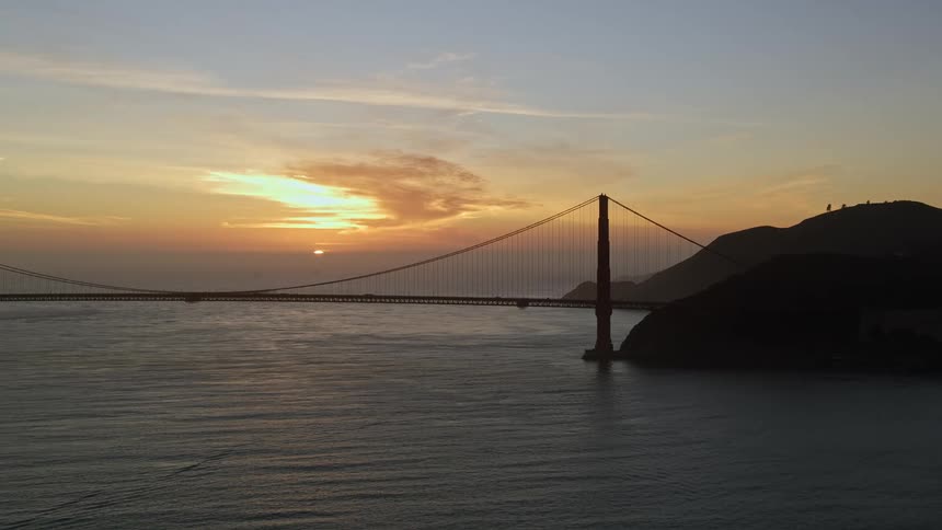 Aerial landscape of a long metal bridge over a vast sea with orange sky