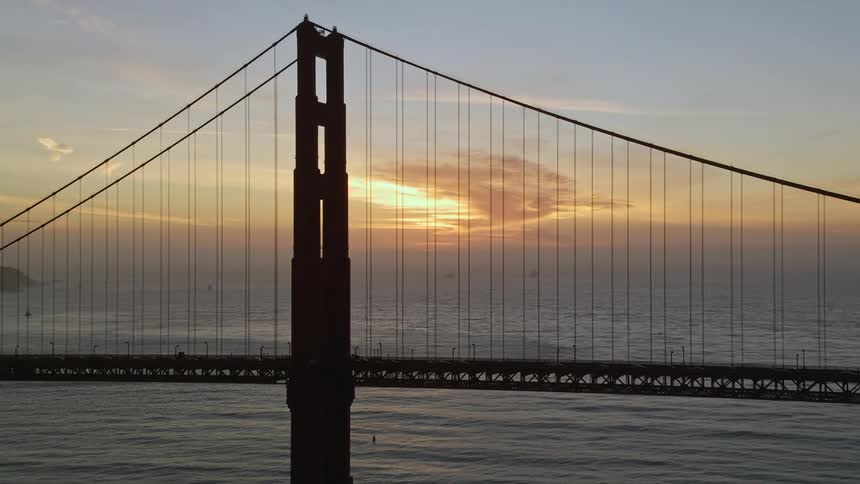 A huge suspension bridge over the sea and the sky is orange