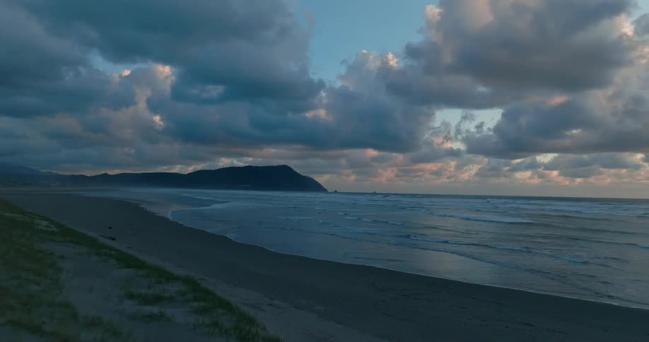 A serene beach scene at dusk with a darkened sky calm waters and a distant cliff