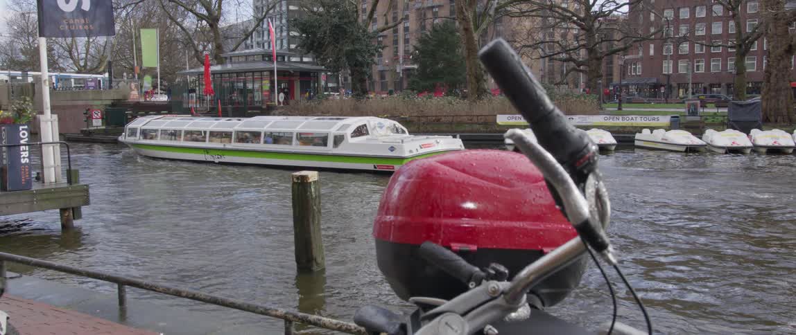 A bicycle parked in front of a canal with a boat or ferry in the city