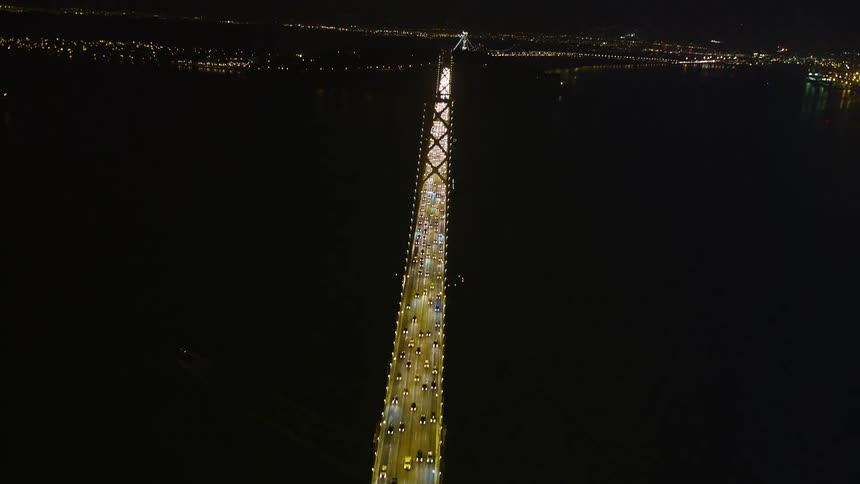 Aerial panorama of a long bridge over the sea illuminated at night and with vehicle traffic