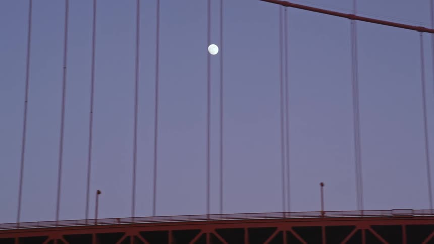 Full moon sets near suspension bridge