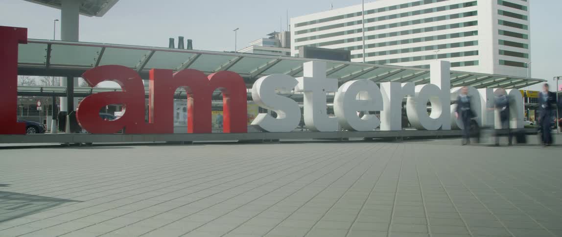 People walking in front of a large i am sterdam red and white sign