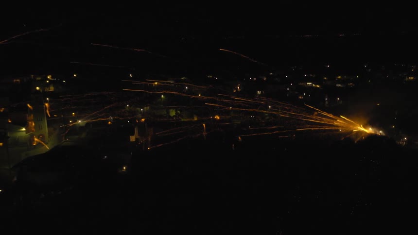 A stream of fireworks shoot out low over a city