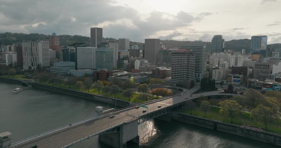Traffic drives over a river bridge and into a downtown area of a city