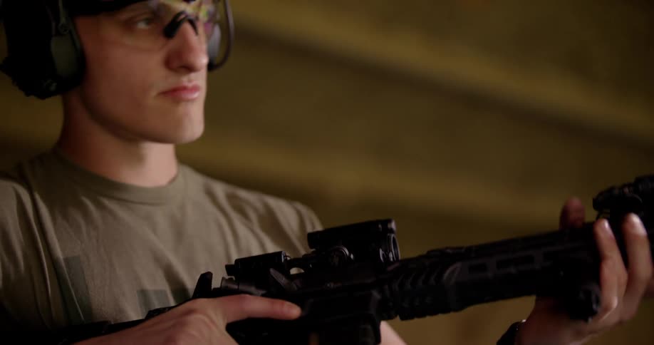A man with goggles is holding a black rifle and is reloading and then shoots