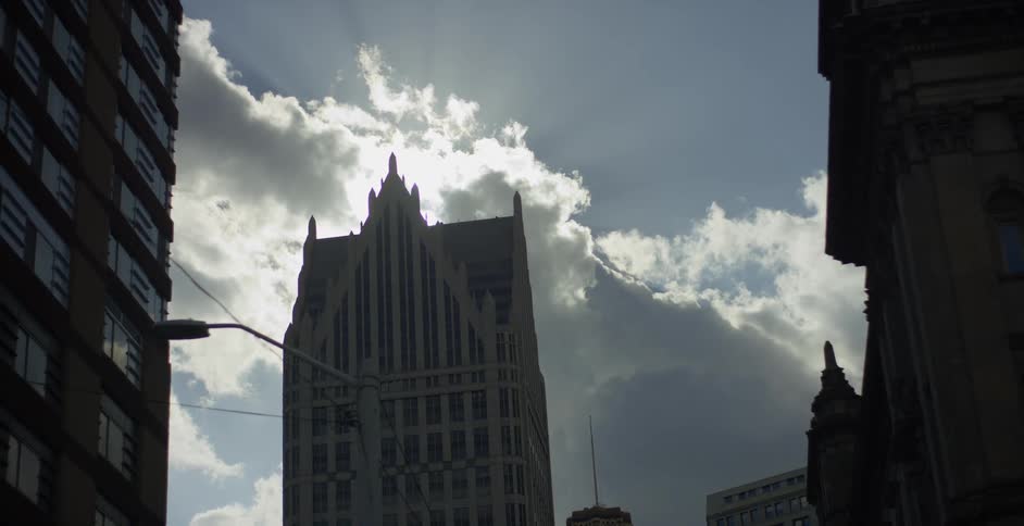 Sun shines through the clouds behind a tall church in a city