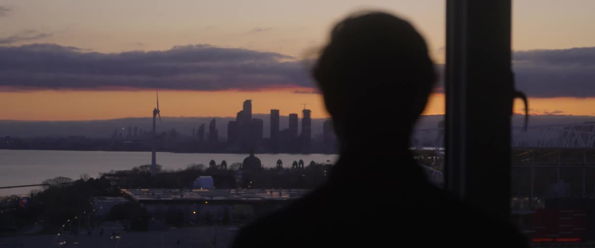 A silhouette of a person standing in front of a window with a city skyline in the background