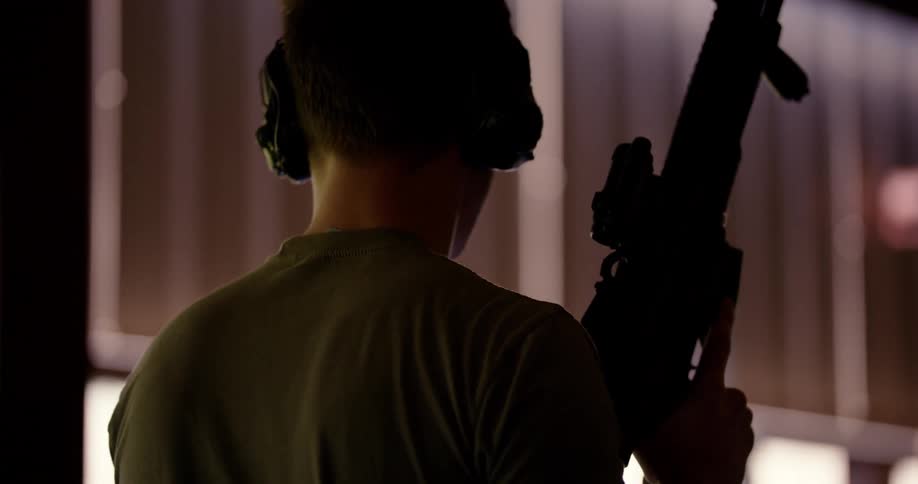 Person seen from behind walking in a dark environment holding a gun pointed upwards