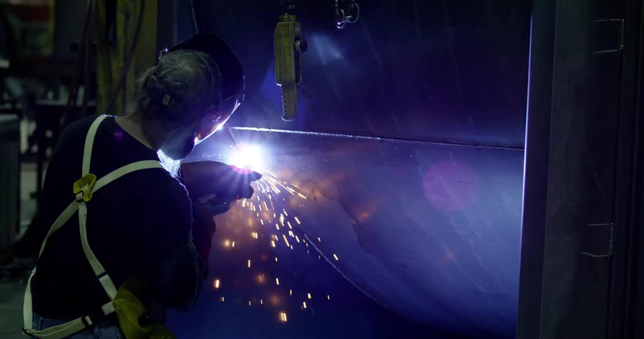 A person wearing safety gear in a workshop welding a large metal structure with sparks flying