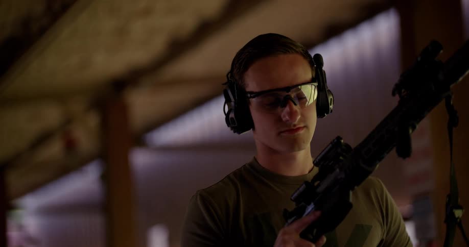 A man wearing protective glasses is walking holding a black rifle