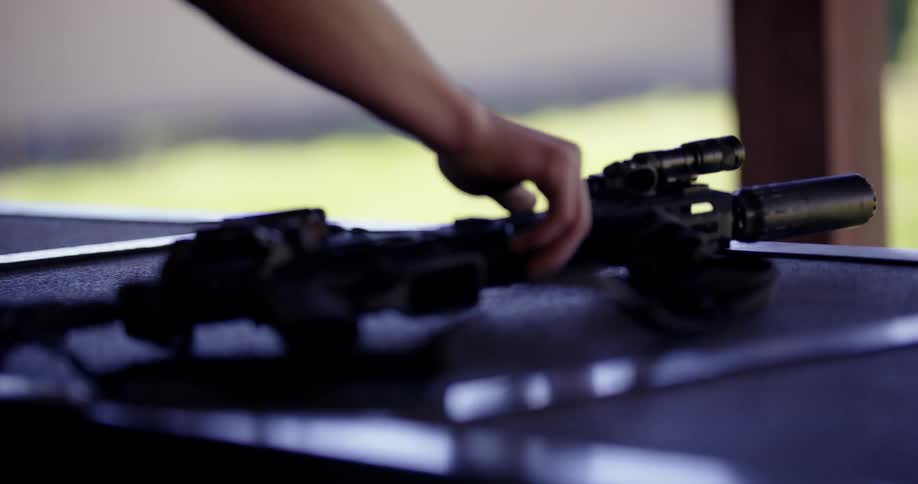 A human hand placing a black rifle on a blue table