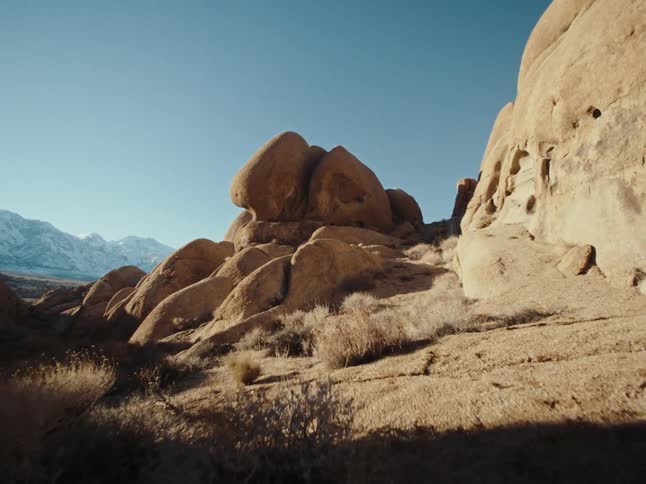 Stone formations tower over field of vegetation across plain from snowy mountains