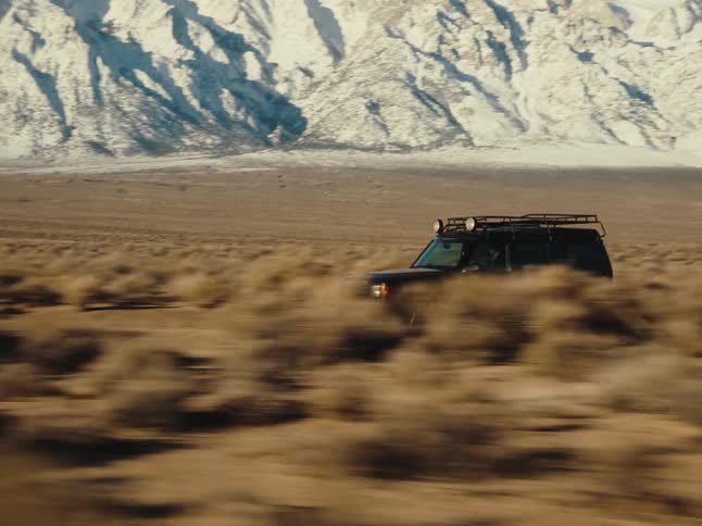 A black offroad car driving on a dirt road next to ice mountains
