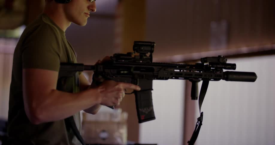 Man loads an automatic rifle and braces it against his shoulder before firing