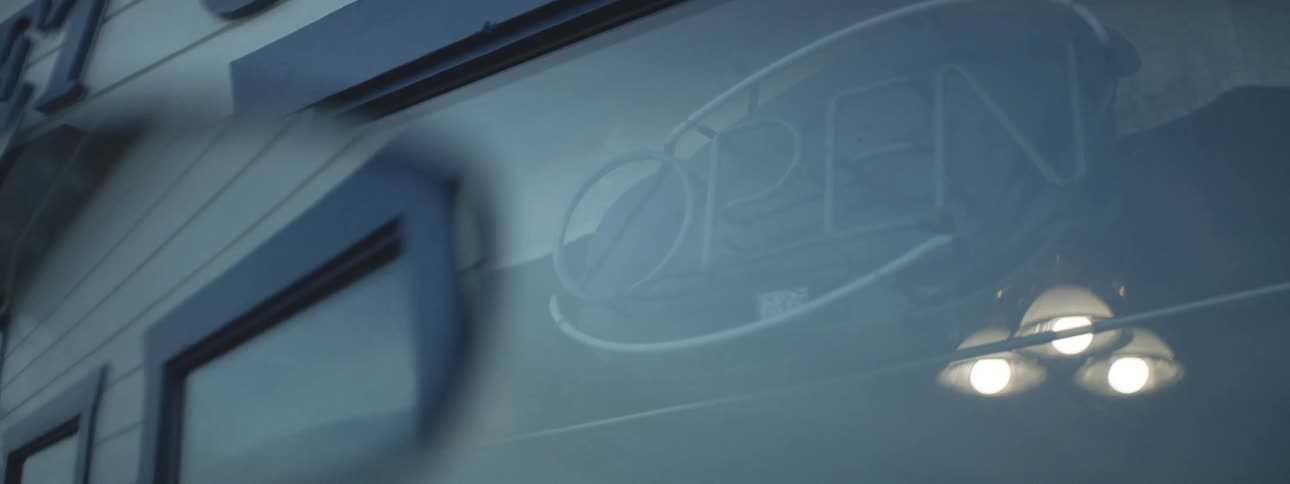 View from outside of a sign with neon lights lighting up with the writing open