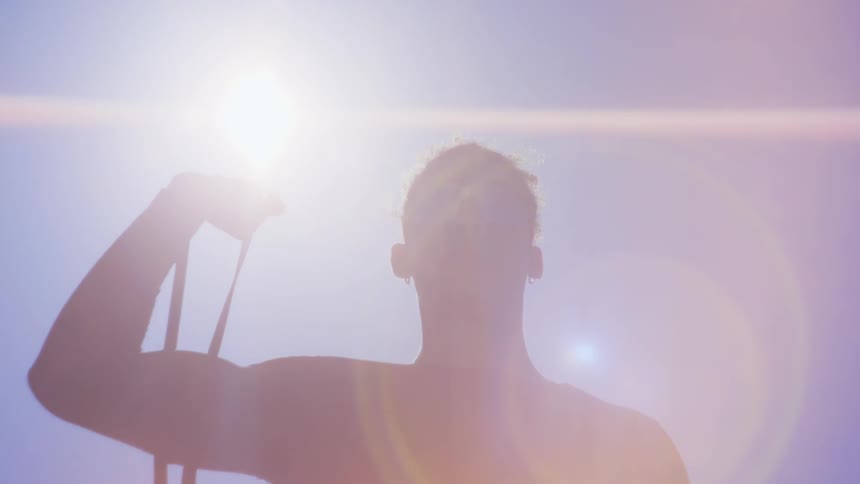 Man with glasses in the sun and using an elastic band stretching his arm upwards against the reflection of sunlight