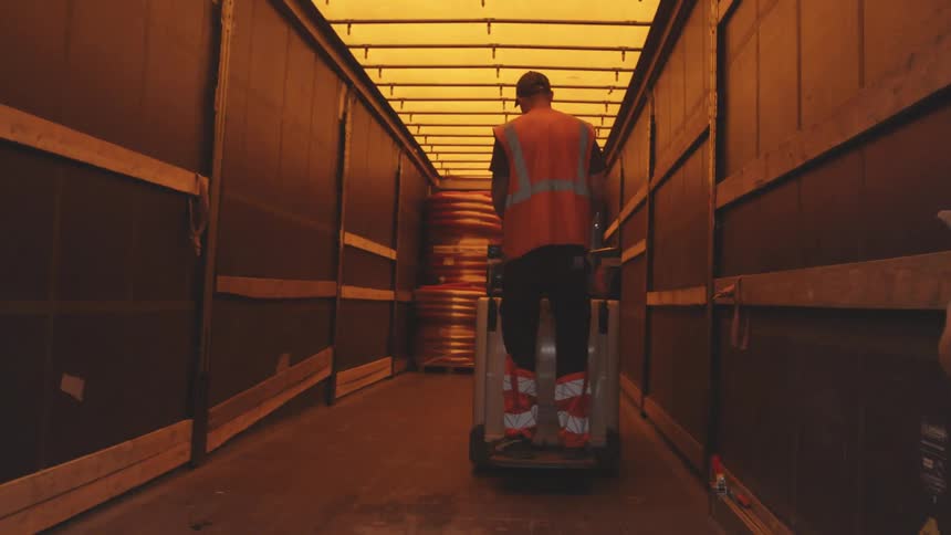 Man in orange vest driving a car with a pallet box towards a container