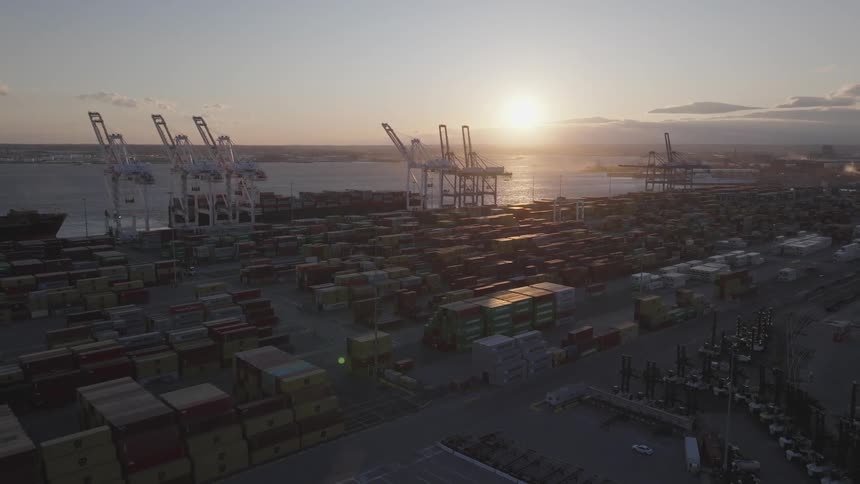 Aerial panorama of a port with stacks of containers on the waterfront with sunrise on the horizon