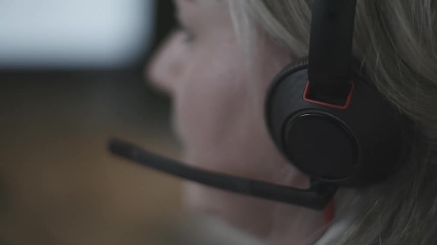 Side portrait of a blonde woman using headphones and typing on a computer keyboard