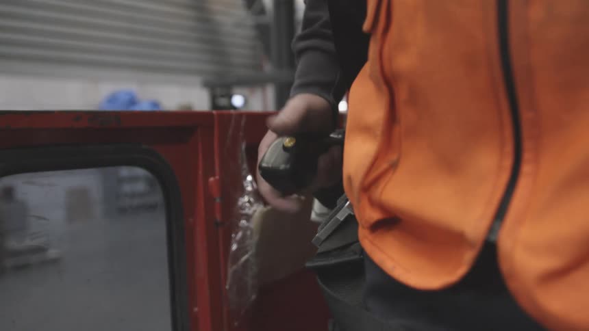 Hands of a man in an orange vest riding a machine inside a factory