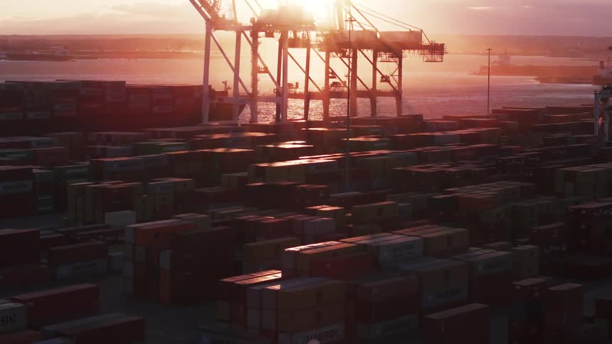 A shipping yard at sunset with containers and cranes next to the ocean
