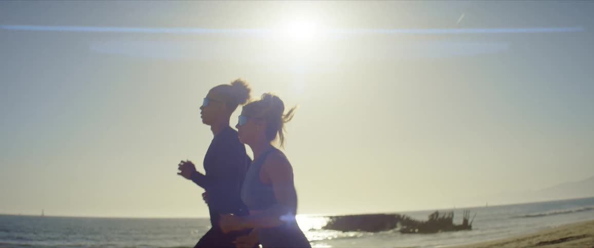 Man and woman with sunglasses running together on the beach sand
