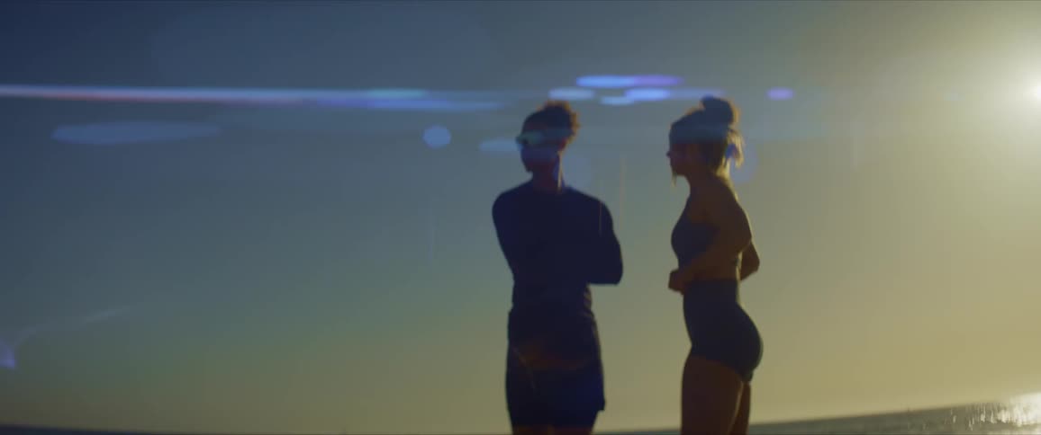 Man and woman with sunglasses on the beach by the sea talking and the sun on the horizon